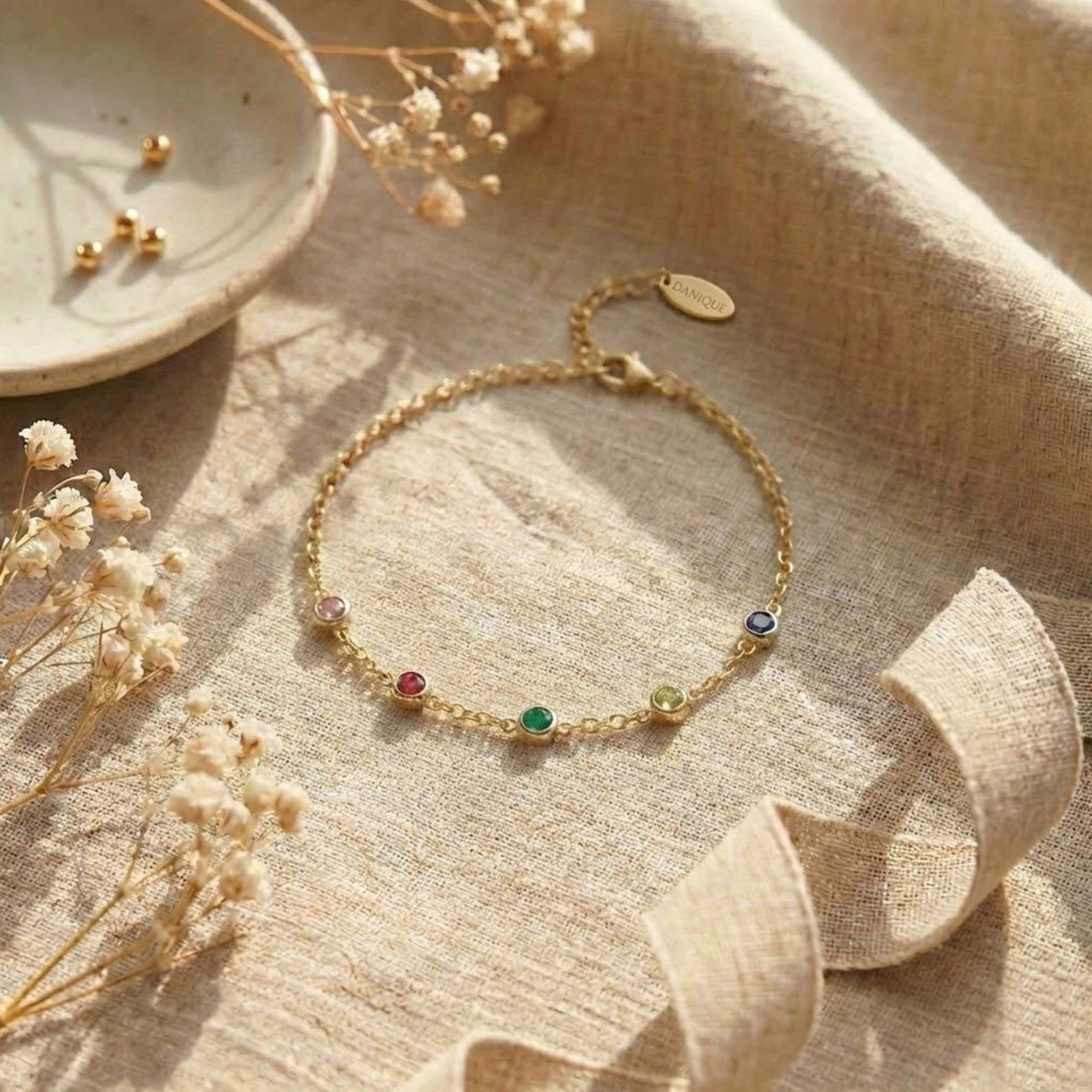 Minimalist personalized birthstone bracelet displayed on neutral linen background, featuring small bezel-set gemstones spaced along a delicate adjustable chain. Custom family bracelet designed with children’s birthstones, available in sterling silver, yellow gold, or rose gold. Thoughtful jewelry gift for mom or grandma, perfect for everyday wear and meaningful occasions.