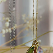 The camera pans down to reveal one silver and one gold teardrop pendant necklace with smaller teardrops on either side. A person runs their thumb down the pendant of the gold necklace to show size and movement. A person wearing a black shirt wears the gold necklace with a large citrine and a small kyanite and ruby. A person shows a silver necklace in an open red danique jewelry gift box. Perfect for christmas, mother's day, anniversaries or birthdays for mom or grandma