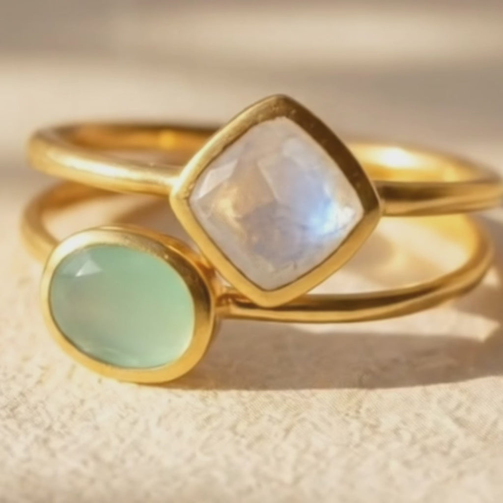 Close-up video thumbnail of oval green chalcedony and diamond-shaped moonstone stacking rings in gold