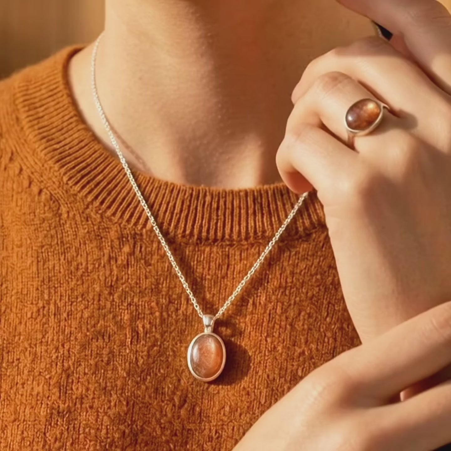 Video showcasing aSunstone necklace displayed on a warm stone surface, featuring an oval orange gemstone pendant in a gold bezel setting on a delicate gold chain.