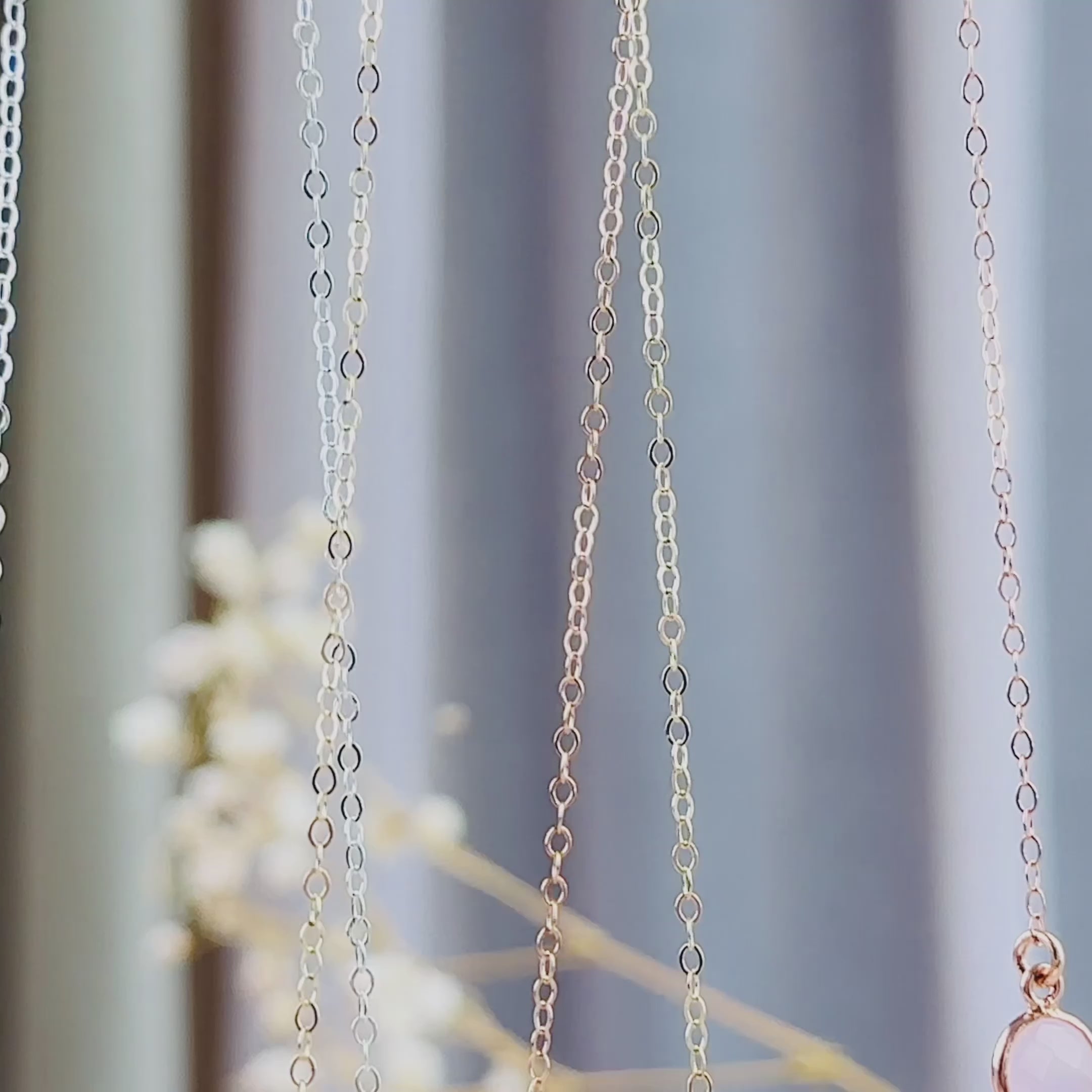 The camera pans down to reveal 3 bar necklaces with connected round birthstones, in silver, gold and rose gold. A person in a white shirt with long brown hair wears a gold bar necklace with "leighton" and a set of footprints engraved on the front with an attached yellow topaz citrine quartz birthstone. An up close shot of the bar pendant is shown. Finally, a silver bar necklace with an attached green amethyst birthstone is revealed in an open danique jewelry box. 