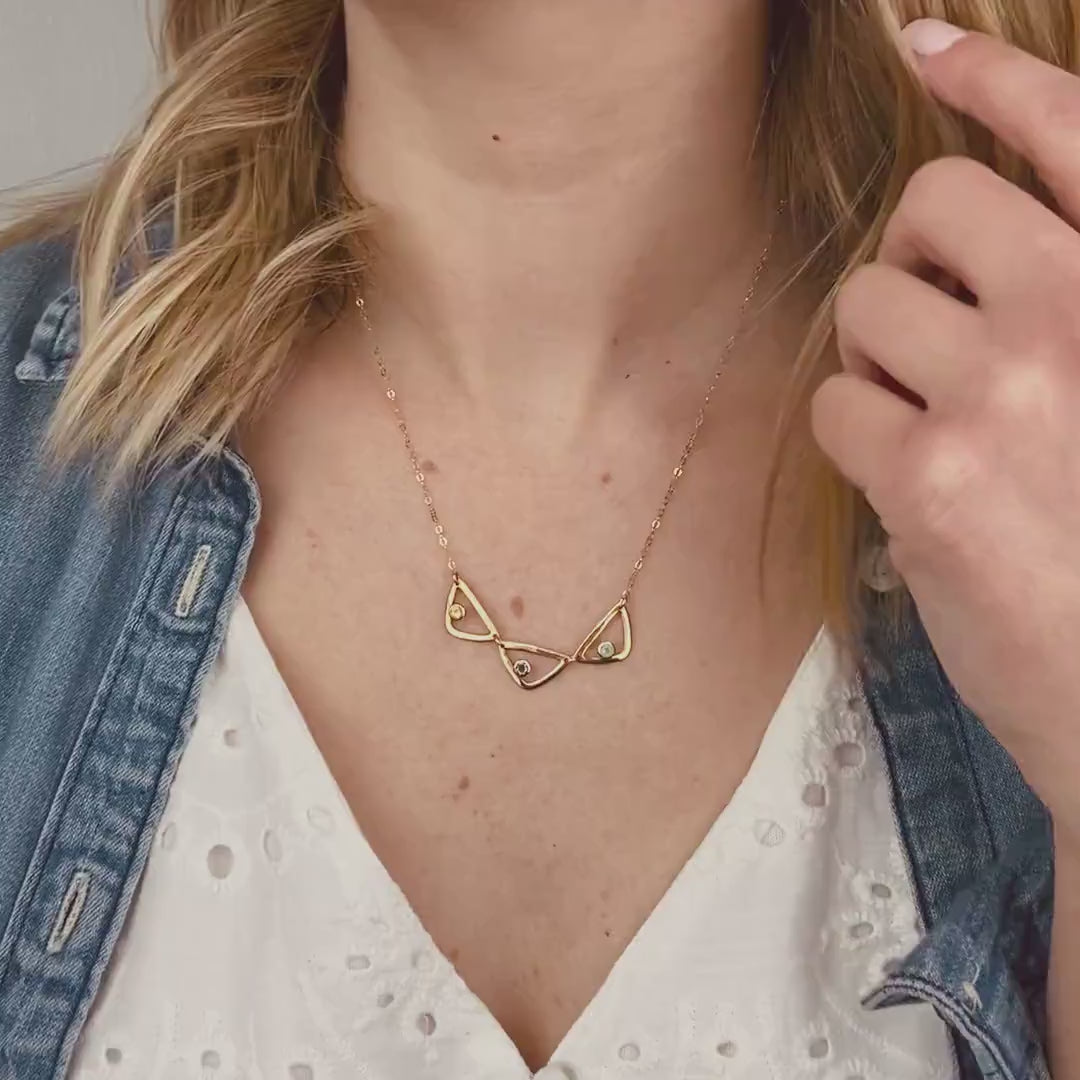 Video of Model in white top is wearing a gold filled open triangle geometric necklace with citrine, purple amethyst and aqua chalcedony birthstones