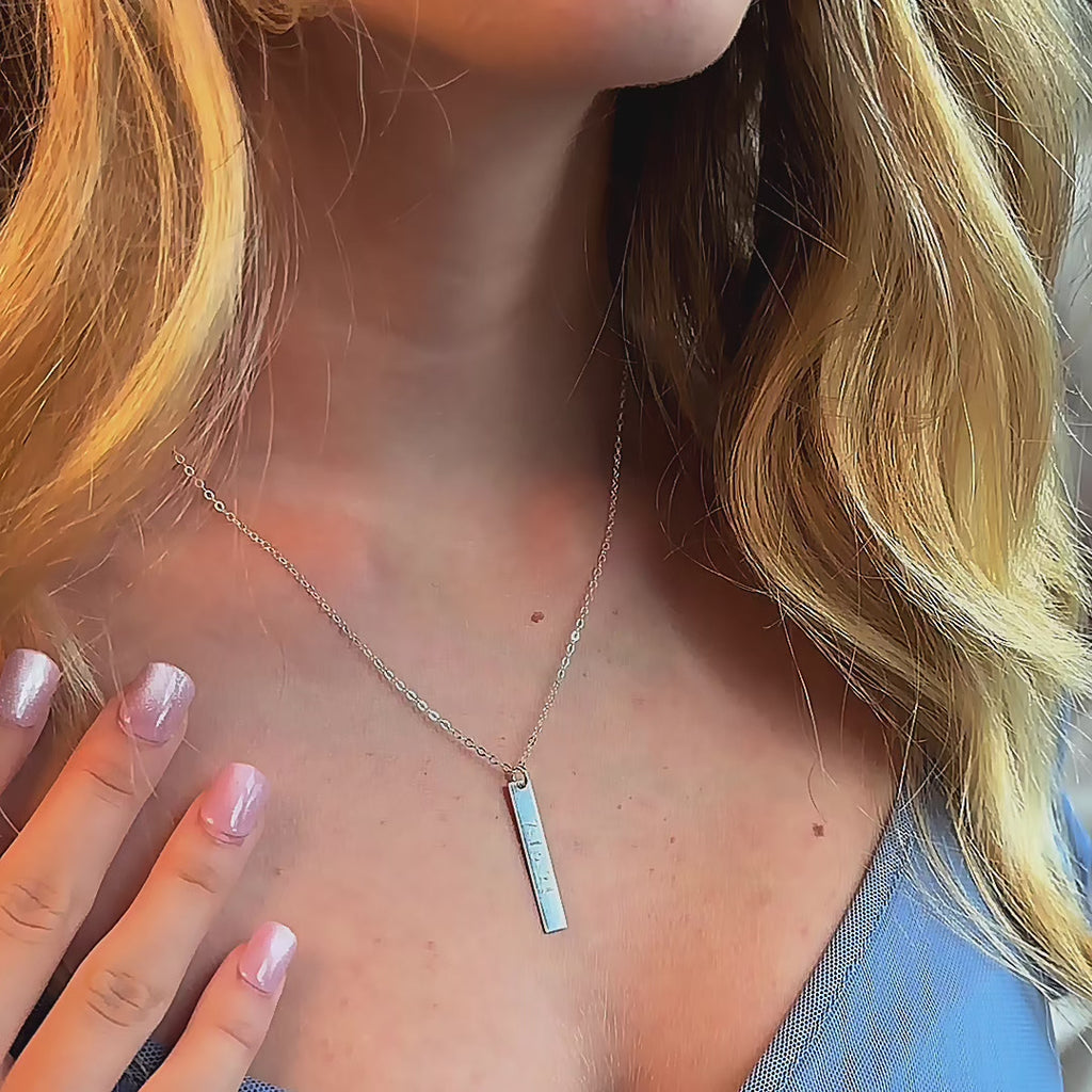 Video showing a sterling silver engraved vertical bar necklace on a model—slim personalized pendant (date, coordinates, or name) on a dainty chain; minimalist, layer-friendly everyday jewelry and an elegant anniversary, bridesmaid, or birthday gift.