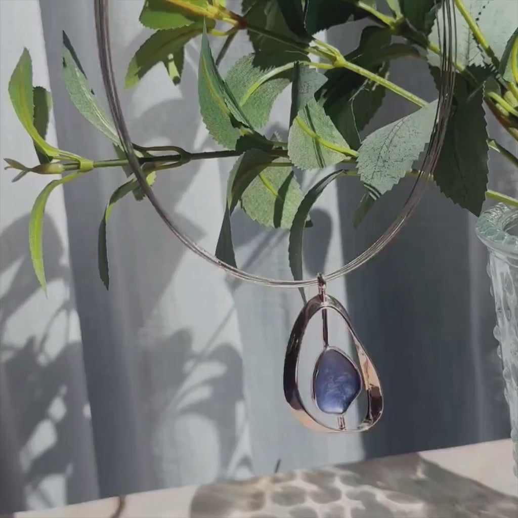 A boho Anima style necklace - an open framed oval pendant with a rod through the center holding a blue metal slab - hangs against a leafy green backdrop. A person's hands hold a pair of matching stud earrings which reflect in the sun. A panover of a barrette style pendant necklace with matching elongated dangle earrings. A panover of a large oval pendant necklace and matching earrings. A blue and rose gold set is followed by a green and silver set. Boho jewelry gift for girlfriend, Christmas gift for wife.