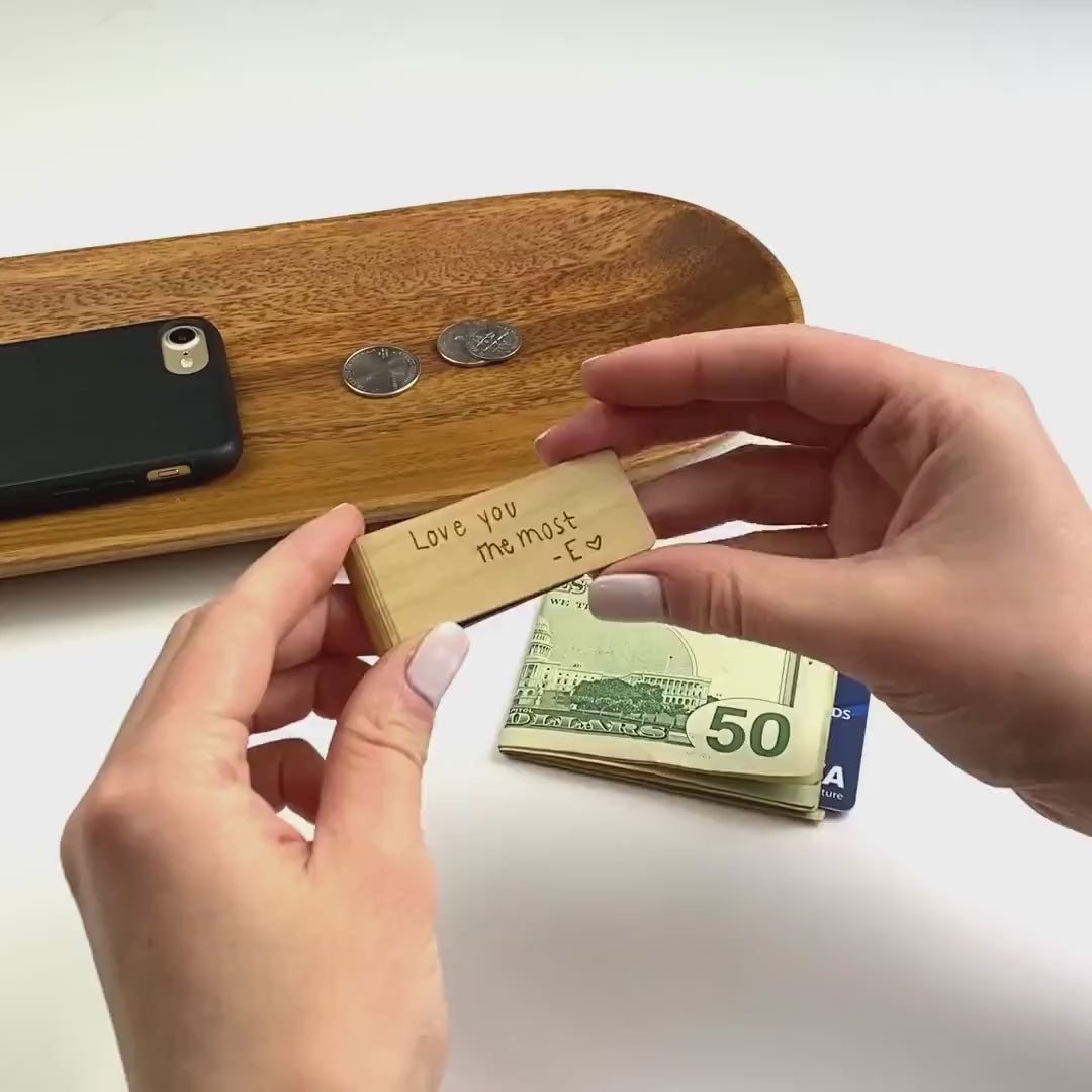 A person holds a birch wood money clip engraved with handwriting reading "Love you the most - E (heart)". These money clips can be made in one of 6 wood finishes. Engravings are applied via laser engraving machine and last a lifetime. Perfect as Father's Day gifts, gifts for Dad, Grandpa or Brother. Money clips are hand crafted with care and are the ideal traditional gift to last a lifetime or even through several generations with the proper care. Custom images can be engraved as well as plain text.