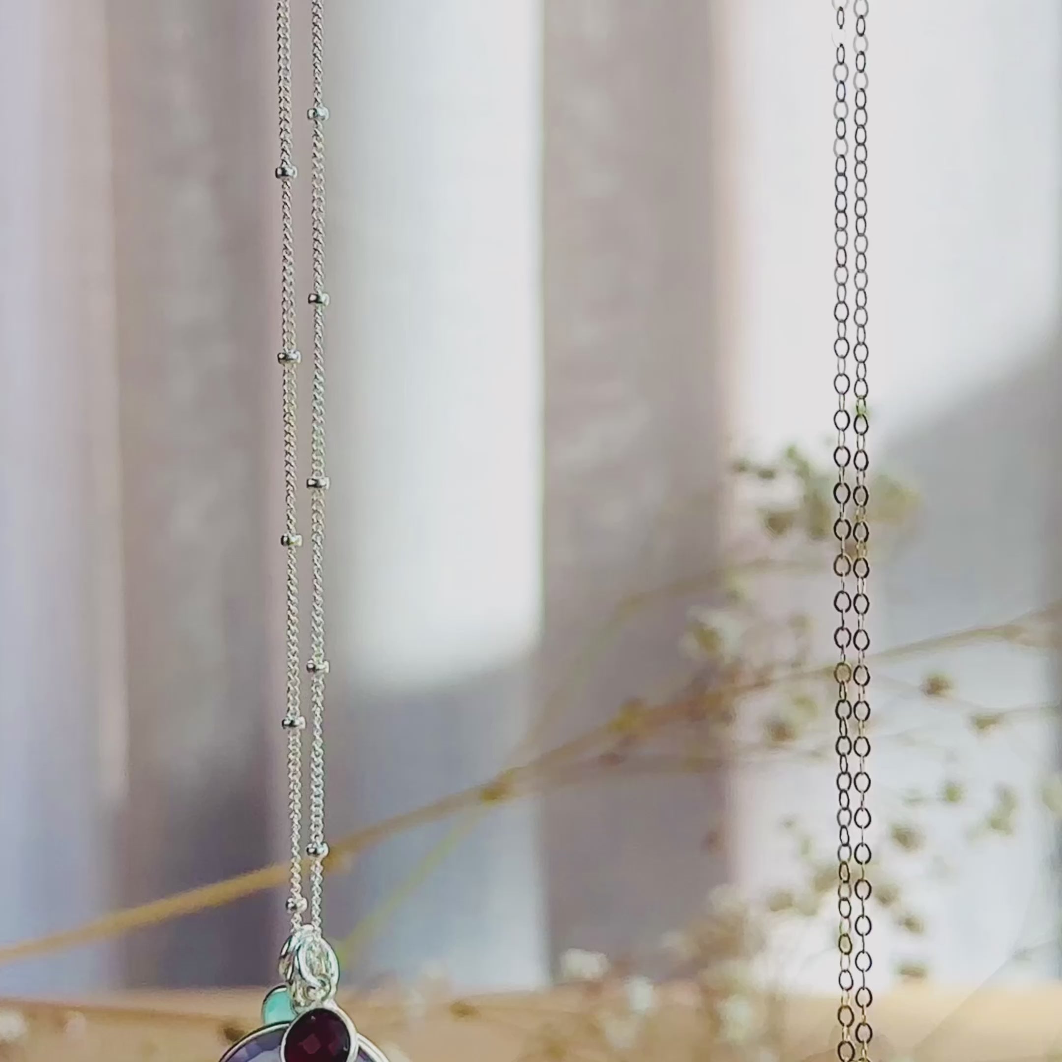 The camera pans down to show a silver and a gold round mother and child pendant necklace. A person wears a gold moonstone necklace with two small stones in pink chalcedony and kyanite quartz. A person shows an up close of the moonstone necklace to show the vibrant blue flash. A silver necklace is in an open Danique Jewelry gift box. This necklace is perfect for christmas gift, mother's day gift, anniversary or birthday present for mom or grandma