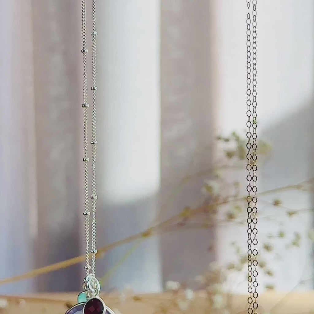 The camera pans down to show a silver and a gold round mother and child pendant necklace. A person wears a gold moonstone necklace with two small stones in pink chalcedony and kyanite quartz. A person shows an up close of the moonstone necklace to show the vibrant blue flash. A silver necklace is in an open Danique Jewelry gift box. This necklace is perfect for christmas gift, mother's day gift, anniversary or birthday present for mom or grandma