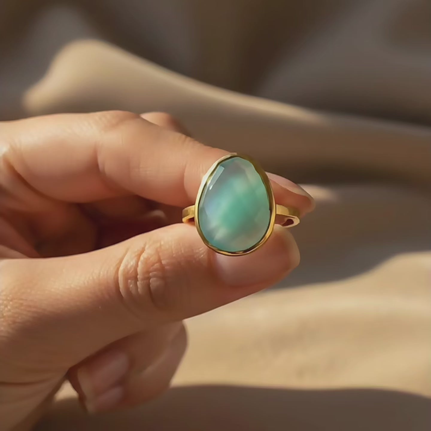 Video showing a pear-shaped aqua chalcedony ring in a gold bezel setting, held in hand in warm natural light to highlight the soft blue gemstone and delicate band.