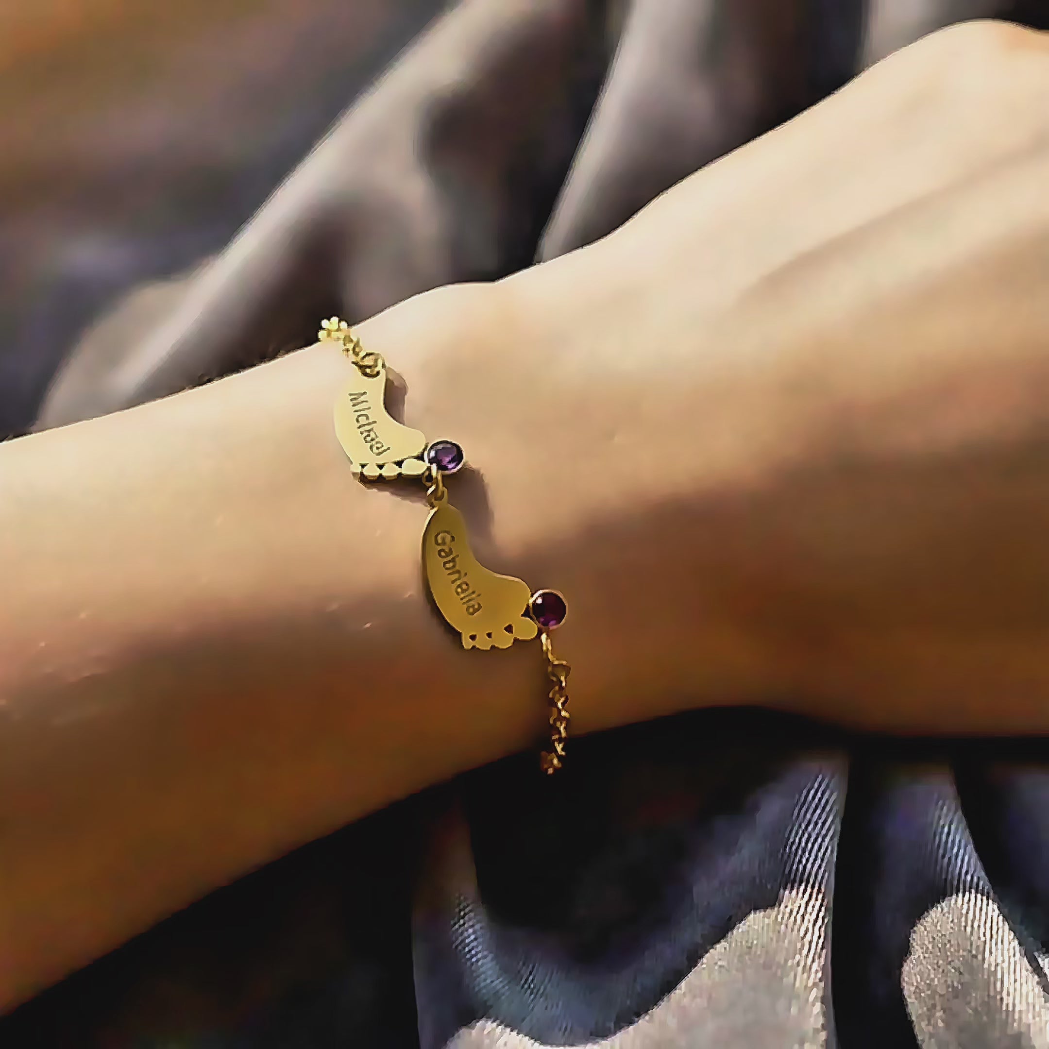 Video showing a gold footprint bracelet with custom engraved baby names “Michael” and “Gabriella,” each paired with personalized birthstones, displayed on a wrist in soft sunlight. Perfect custom mom bracelet, new mom gift, birthstone jewelry, and personalized family keepsake.