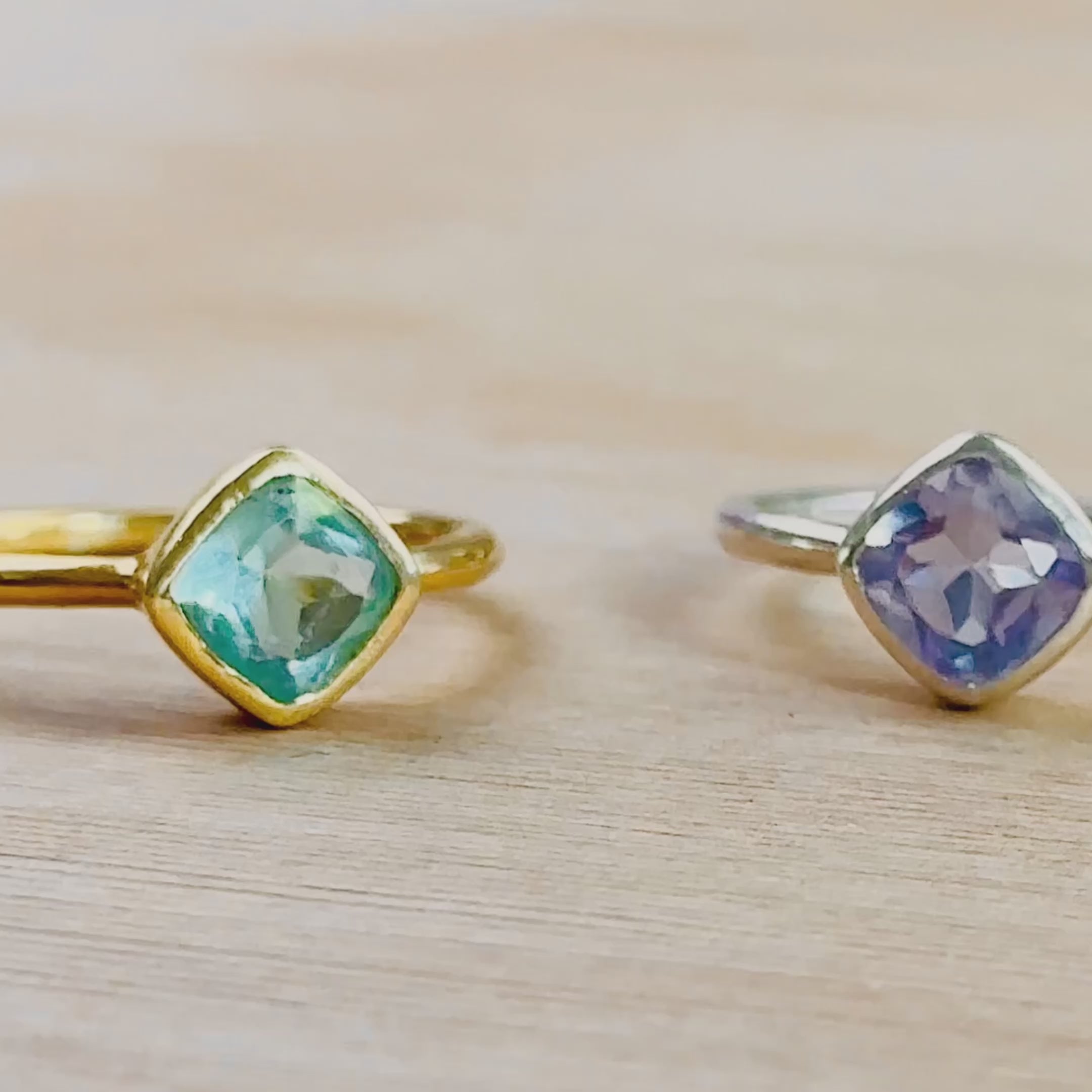 A camera pans horizontally to reveal blue topaz, alexandrite and clear quartz diamond rings. A person holds a gold set blue topaz diamond shaped ring up close. A person wears a gold moonstone ring on their pointer finger in the sunlight. A different person wears a stacked set of two rings in silver with kyanite and alexandrite. The same ring set is then shown in an open red Danique Jewelry box. Ideal for birthdays, Christmas, or as a Mother's Day gift for her.