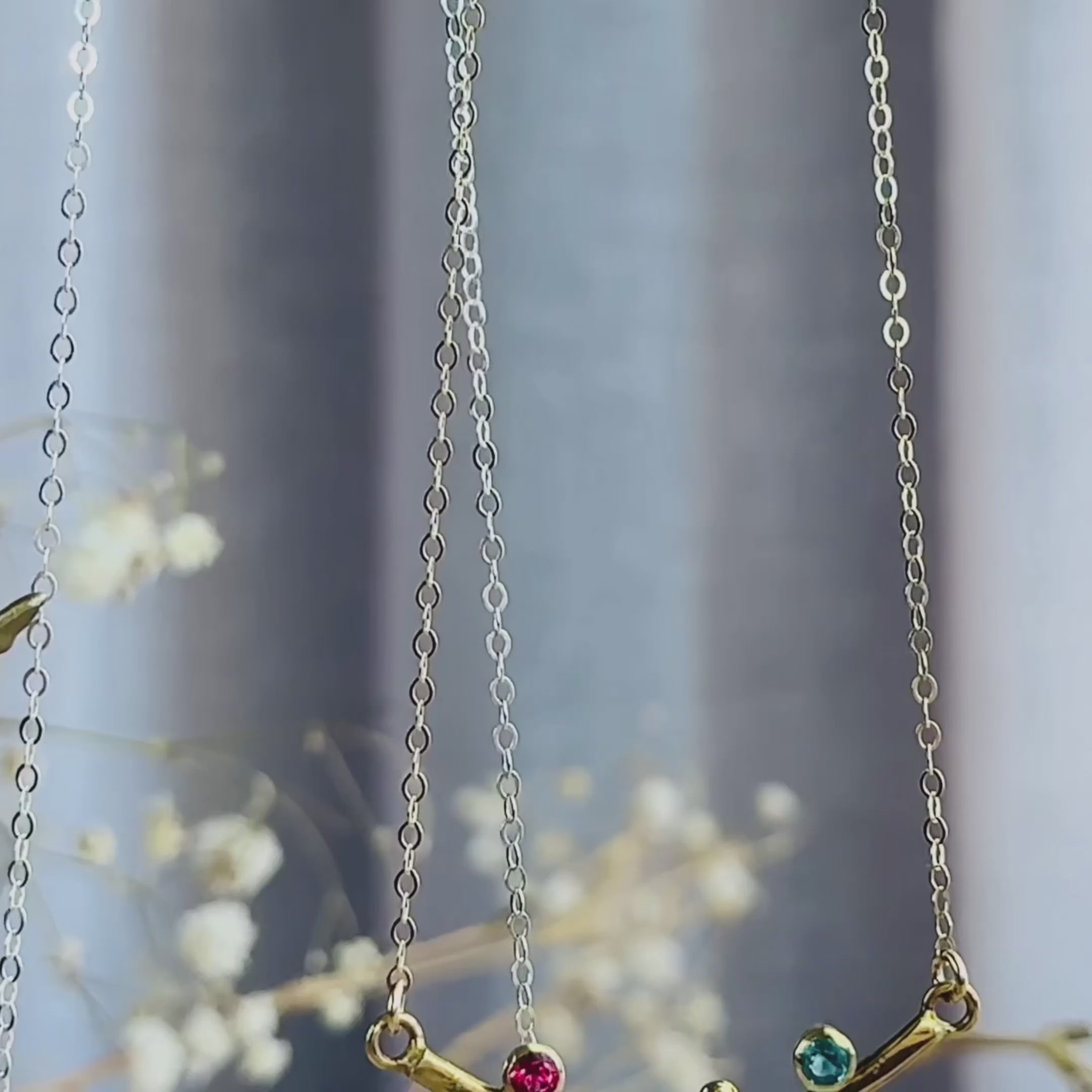 The camera pans down to reveal 2 curved bar necklaces in gold and silver. A close up of a gold curved bar necklace on a person shows the metal gleaming in the sunlight. Two hands hold up a curved bar pendant to show off the set birthstones. A person opens a red Danique Jewelry box to reveal a sterling silver curved bar mother's necklace. Birthstones are available for every month. Metal colors are 925 sterling silver and 18k Vermeil gold. Perfect for Mother's Day, Christmas, or Birthday gifts for Mom Grandma