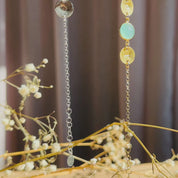 A gold and a silver gemstone charm bracelet dangle against a curtained background. A person holds out a multi birthstone and initial bracelet to show off the checkerboard faceted round stones and gold brushed disc initial charms. A person holds out their arm to show off a gold mother's bracelet. A person opens a red Danique Jewelry box to reveal a silver multi-stone mother's bracelet with children's birthstones and initials. This is the perfect Christmas or Birthday gift for Mom or Grandma from her family.