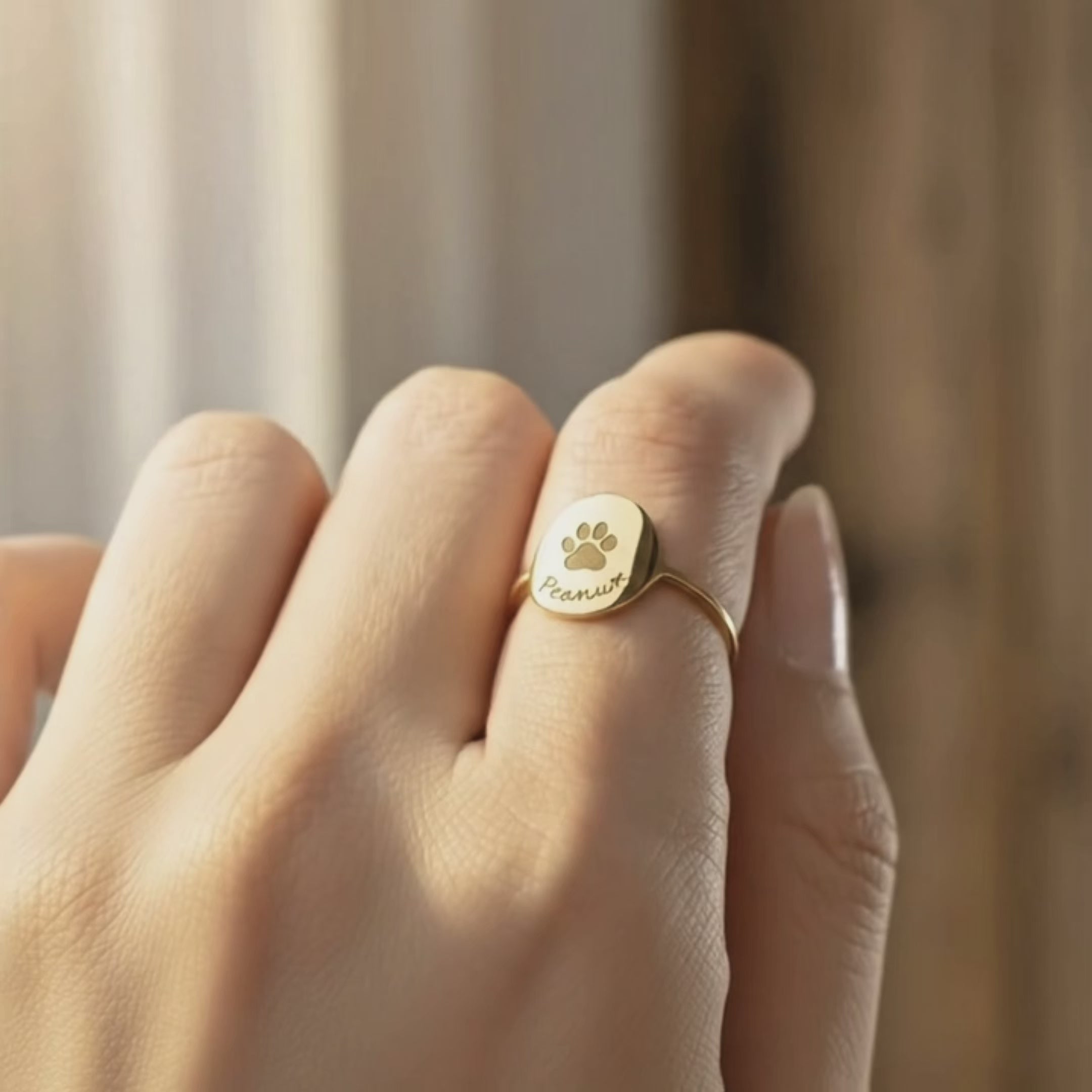 dainty gold paw print ring shown on a hand, featuring a small round signet-style face engraved with a tiny paw print and the name “Peanut” in script underneath, minimalist band that sits comfortably for everyday wear, perfect custom pet lover jewelry to celebrate a dog or cat, meaningful memorial ring or gift for pet parents, available in sterling silver or gold finishes and personalized with your own pet’s name or short word