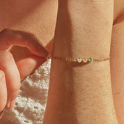Dainty custom birthstone bracelet shown on a woman’s wrist in warm sunlight, featuring three tiny bezel-set gemstones on a delicate gold chain to represent children or family members. Minimalist personalized birthstone bracelet perfect for everyday wear or stacking with other bracelets, a meaningful gift for mom, grandma, daughter or best friend for birthdays, Mother’s Day, Christmas or anniversary.