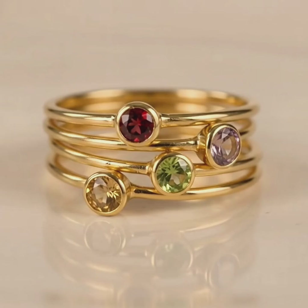A video showcasing a Personalized tiny birthstone round gemstone rings with garnet purple amethyst peridot citrine birthstones vermeil gold plating. Wear them alone of stack them on the same finger