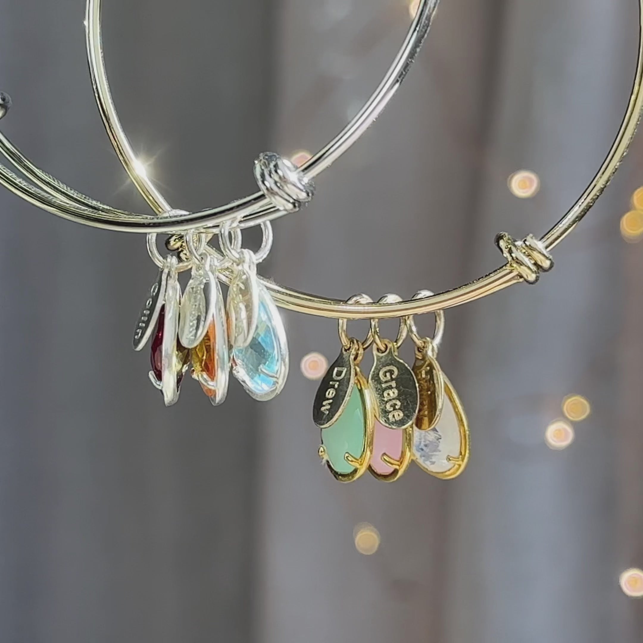 A gold and a silver bangle bracelet with engraved name tag charms and half bezel prong teardrop birthstones. A person wears a gold bangle bracelet with three kids names and birthstones. A silver bangle bracelet in an open red Danique Jewelry box. Personalized bracelet for mom with kids names and gemstones, multi stone multi color charm bracelet bangle style for mother for women