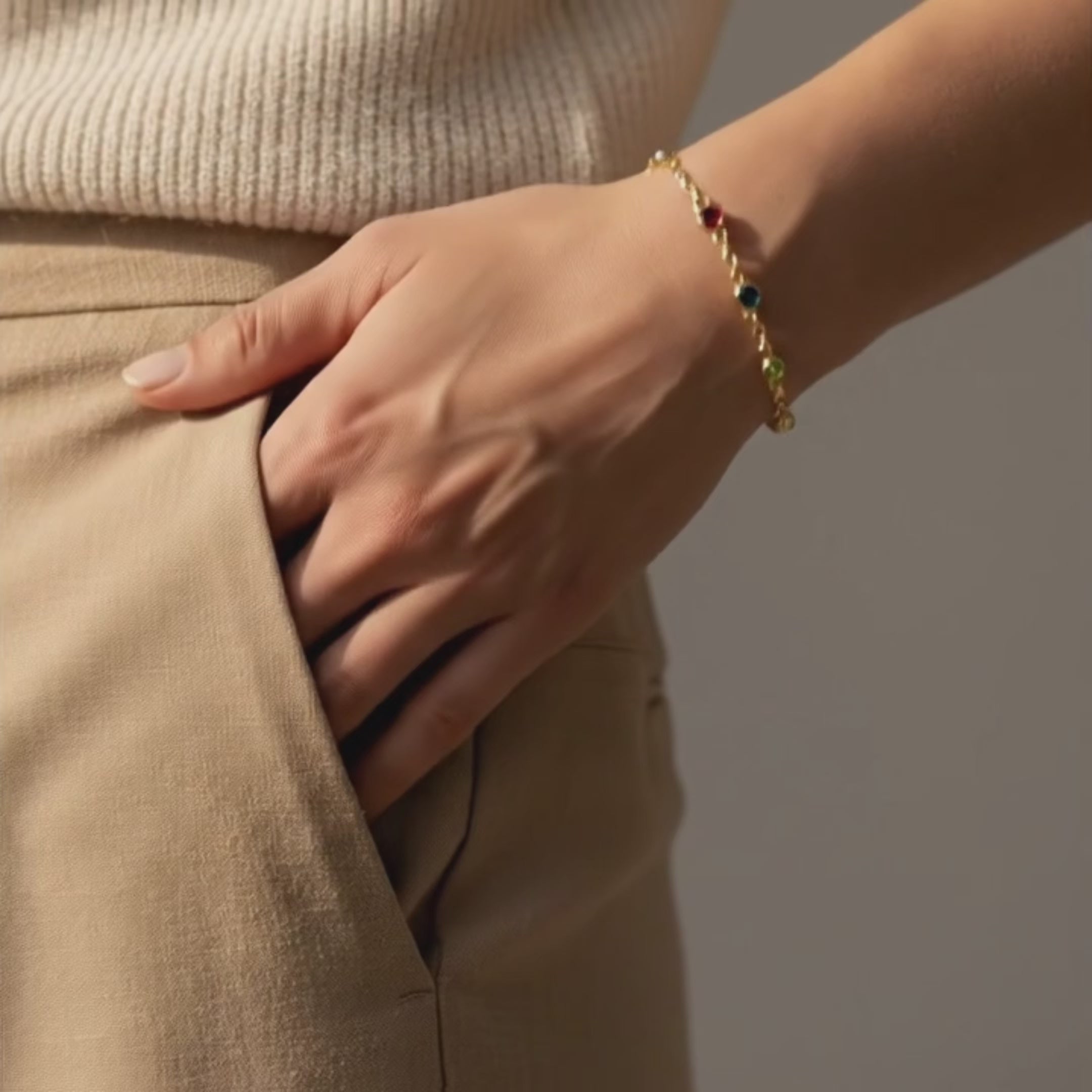 Video showcasing a minimalist custom birthstone bracelet for mom worn on the wrist, featuring delicate gold chain with colorful natural gemstones representing children, styled in a neutral outfit to highlight the dainty personalized family jewelry design.