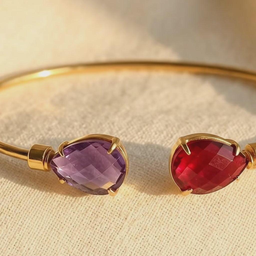 Video showing a personalized birthstone bangle bracelet with two custom faceted birthstones, featuring a purple amethyst and garnet stone in a delicate gold bracelet setting.