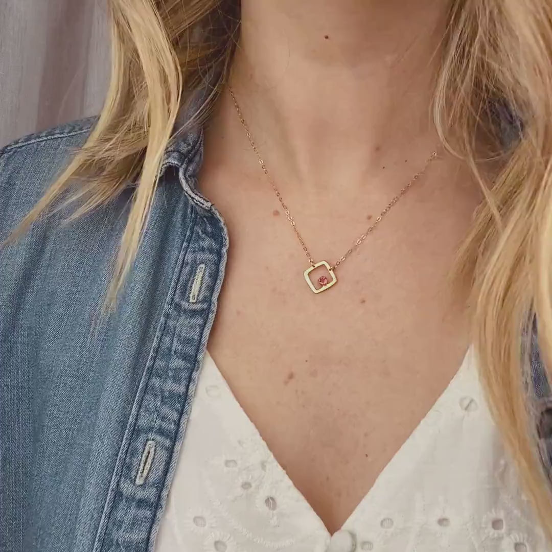 video of Model in white top is wearing a gold plated open square minimalist necklace with ruby birthstone july birthstone.