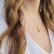 A person wears a gold custom leaf pendant necklace with birthstones. A hand shows an up close shot of a bezel set gold leaf necklace. Two hands open a red Danique Jewelry gift box to reveal a sterling silver plant necklace with custom gemstones inlaid throughout. Perfect for plant moms, nature lovers, or those looking to keep their family's birthstones close.