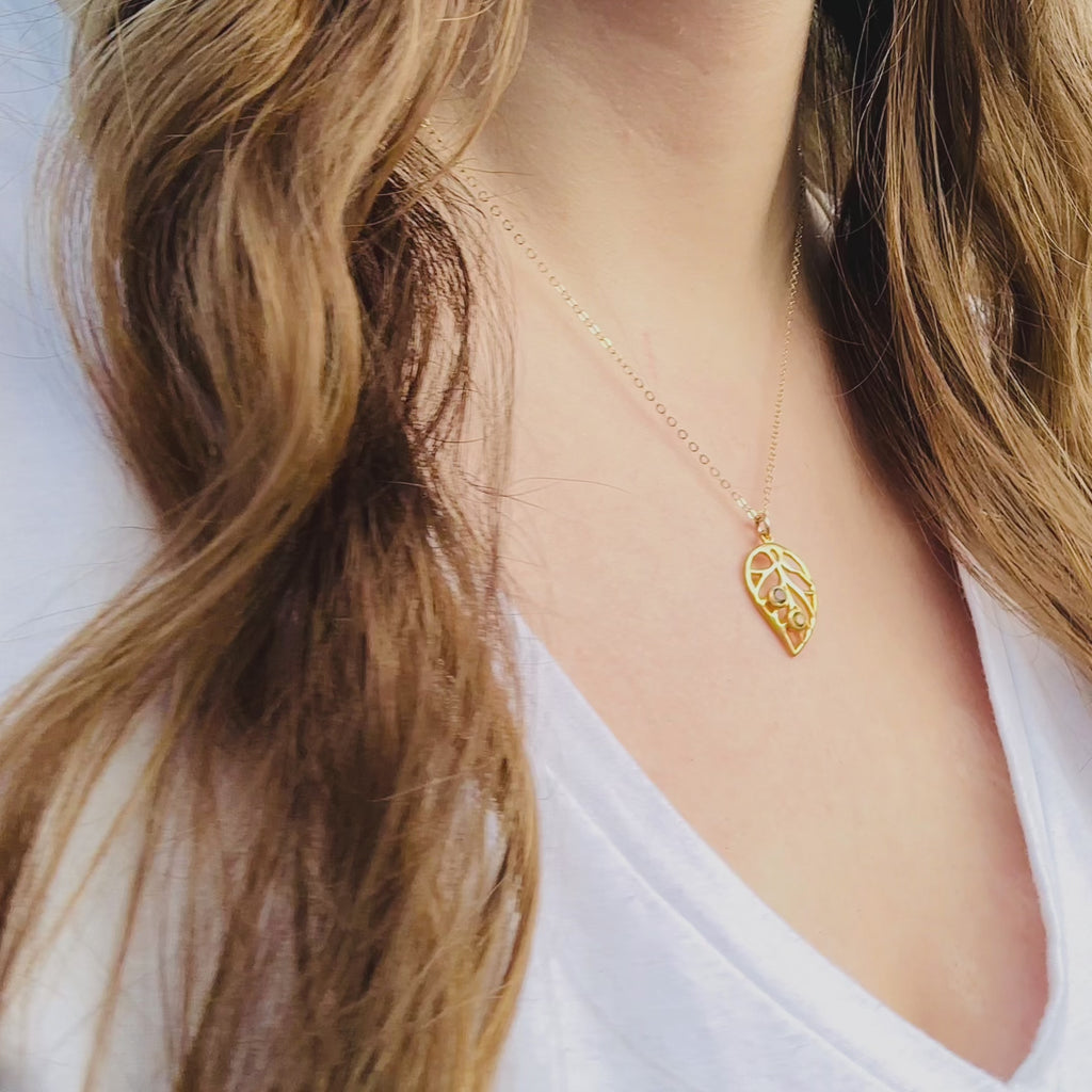 A person wears a gold custom leaf pendant necklace with birthstones. A hand shows an up close shot of a bezel set gold leaf necklace. Two hands open a red Danique Jewelry gift box to reveal a sterling silver plant necklace with custom gemstones inlaid throughout. Perfect for plant moms, nature lovers, or those looking to keep their family's birthstones close.