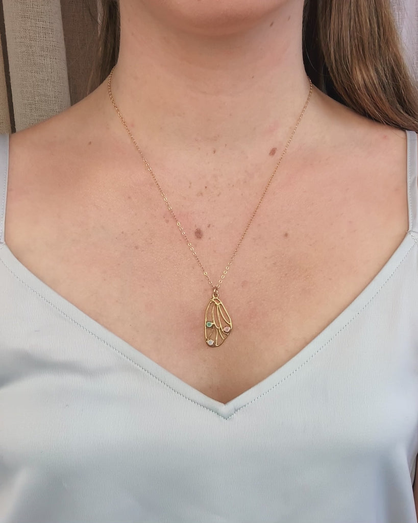 A person in a white silk tank top wears a gold butterfly wing necklace with three birthstones bezel set in the wing with aqua chalcedony (March), Pink chalcedony (October) and moonstone (June). Birthstones available for every month, this can be made with one, two, three, or four birthstones. Metals available are sterling silver, gold filled, and rose gold. This is perfect for day to day wear and shows off the love you hold for your family! Perfect for Mother's Day, Mom's Birthday, or an anniversary gift.