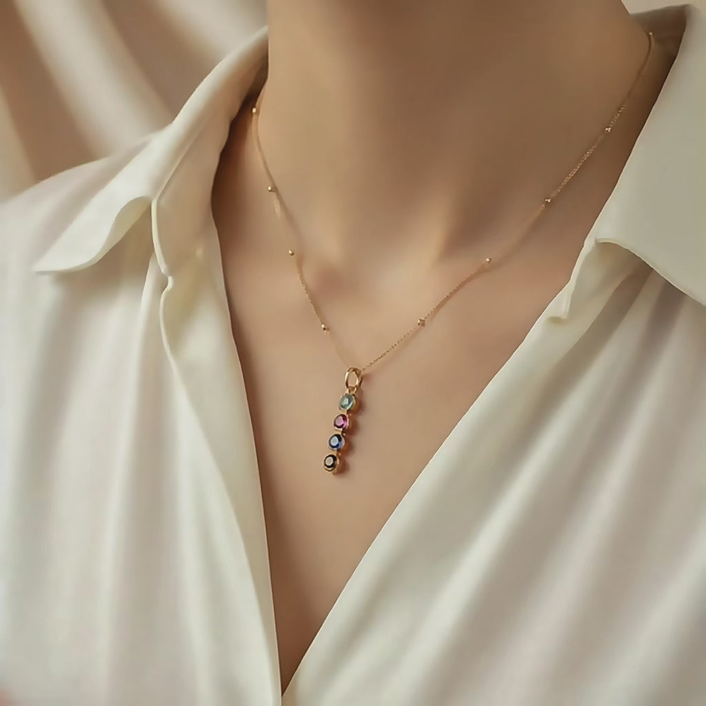 Video showcasing a minimalistic gold mom necklace featuring a vertical row of tiny birthstones, worn with a delicate beaded chain. Personalized family birthstone necklace, meaningful gift for moms, grandmothers, and new moms, elegant minimalist jewelry for everyday wear.