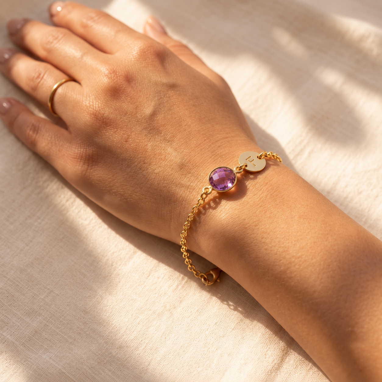 Close-up of personalized purple amethyst birthstone bracelet with initial charm worn on the wrist.