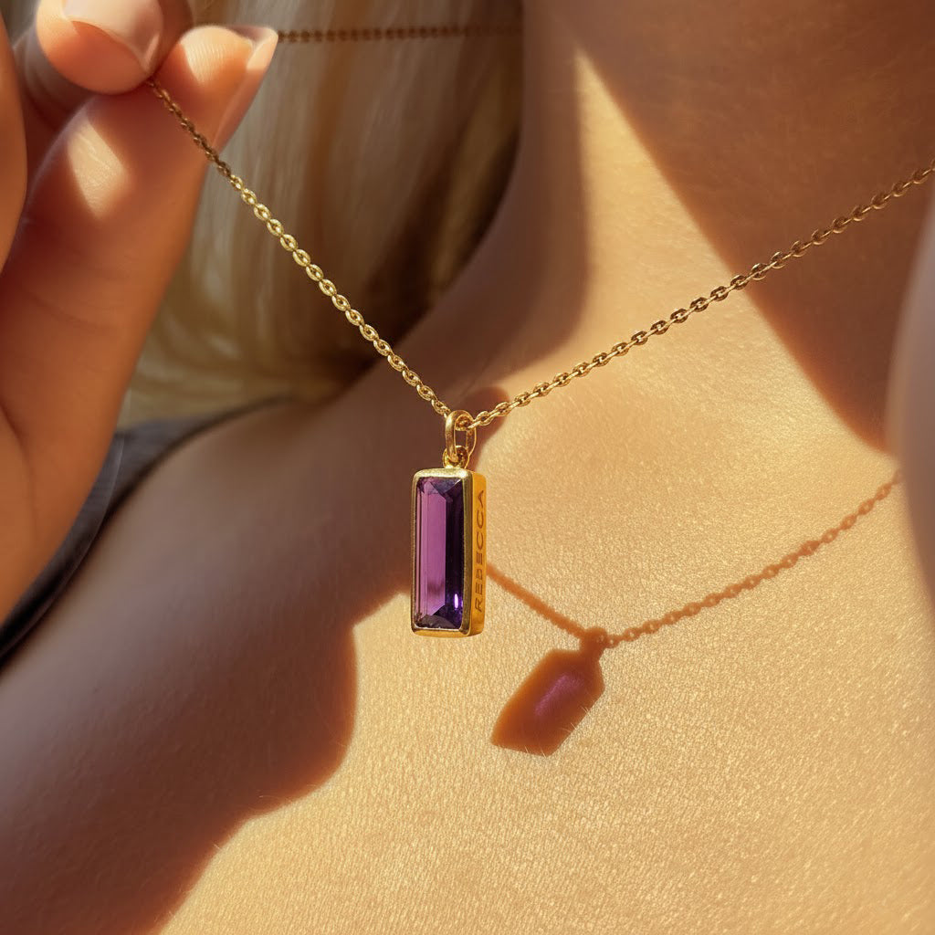 vertical bar name necklace featuring a baguette amethyst bar pendant resting at the collarbone, personalized with subtle side engraving, shown in bright sunlight on gold filled chain for a warm glow, stylish February birthstone bar necklace she can wear every day or dress up for evenings, trending baguette birthstone necklace style that looks beautiful layered with other delicate chains and makes a chic personalized gift for her