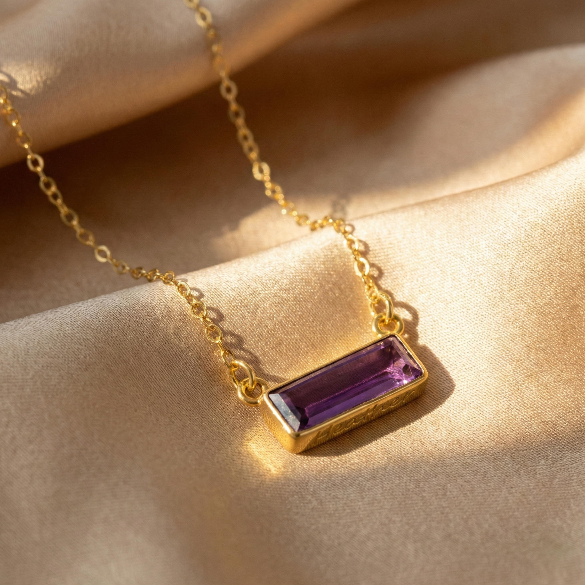 Gold birthstone bar necklace with rectangular purple amethyst stone resting on soft neutral fabric