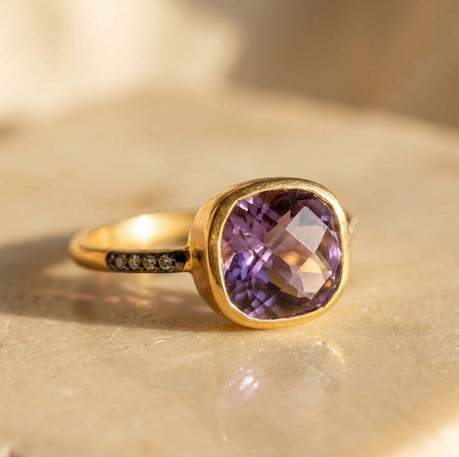 Cushion cut purple amethyst pave ring in yellow gold with faceted gemstone and sparkling accent band.