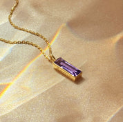 vertical bar name necklace featuring a baguette amethyst bar pendant resting at the collarbone, personalized with subtle side engraving, shown in bright sunlight on gold filled chain for a warm glow, stylish February birthstone bar necklace she can wear every day or dress up for evenings, trending baguette birthstone necklace style that looks beautiful layered with other delicate chains and makes a chic personalized gift for her