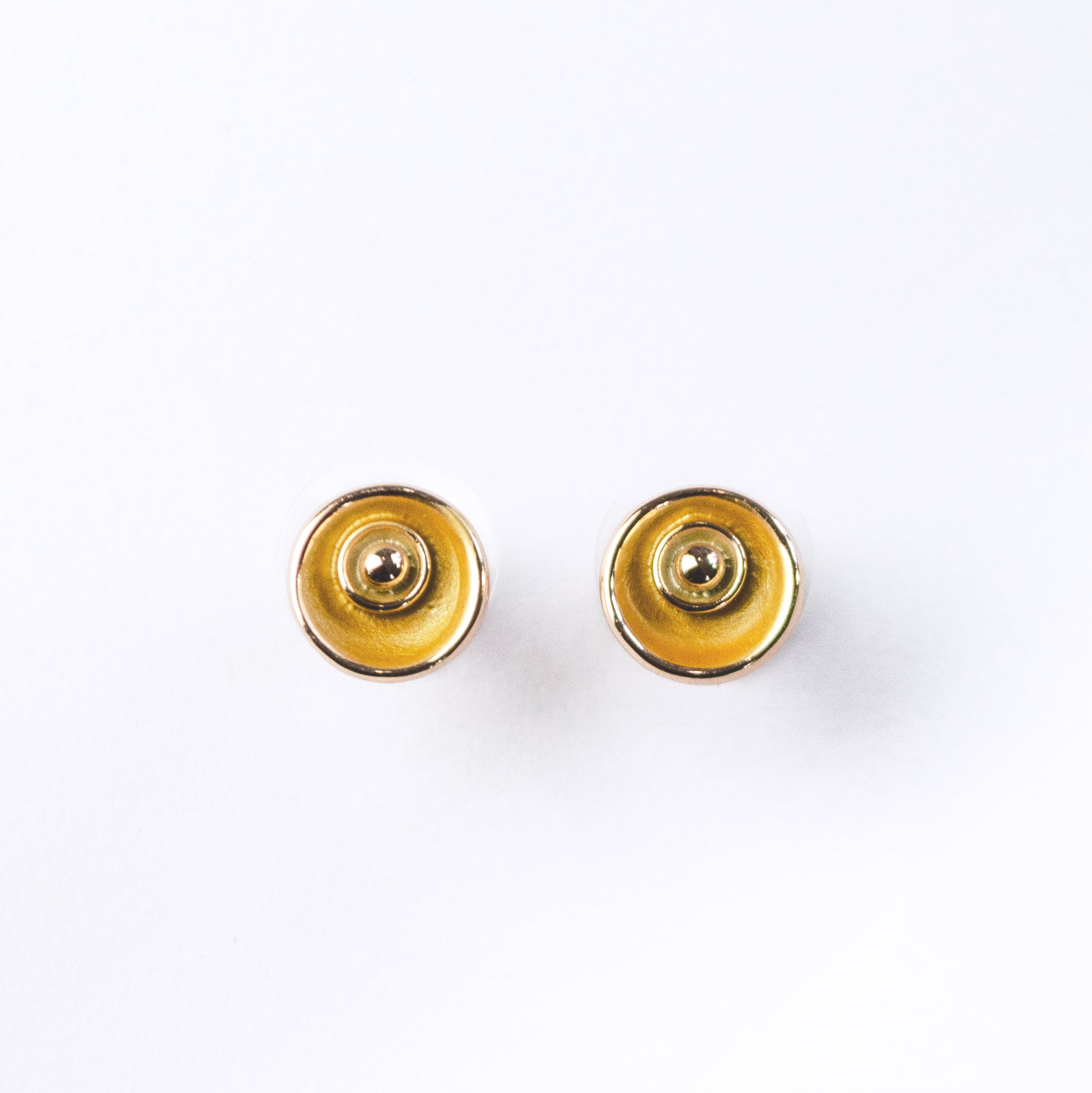 A pair of circular abstract flower earrings against a white background with rose gold plating and painted in gold and beige