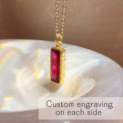Ruby bar pendant necklace with custom engraving shown on a shell in golden sunlight.