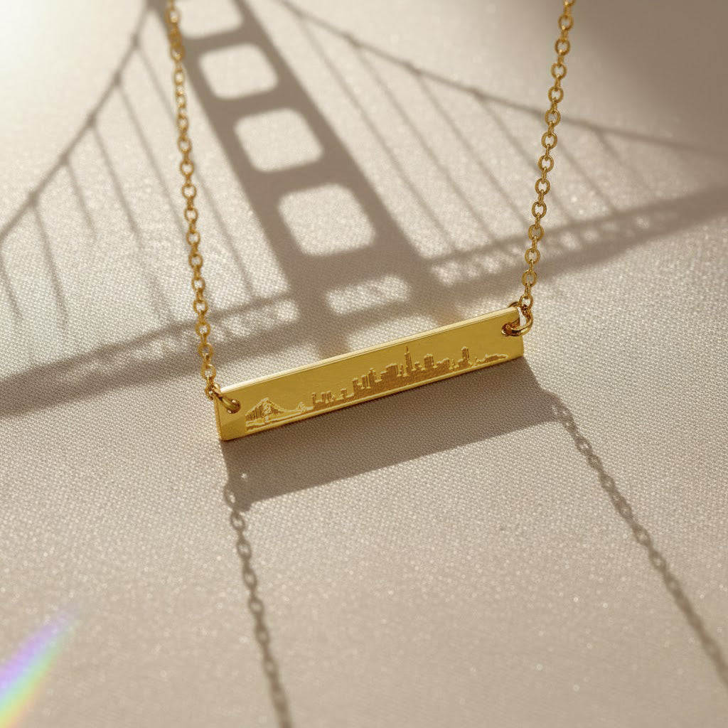 Engraved city skyline bar necklace photographed with Golden Gate Bridge shadow, personalized travel lovers necklace in gold.
