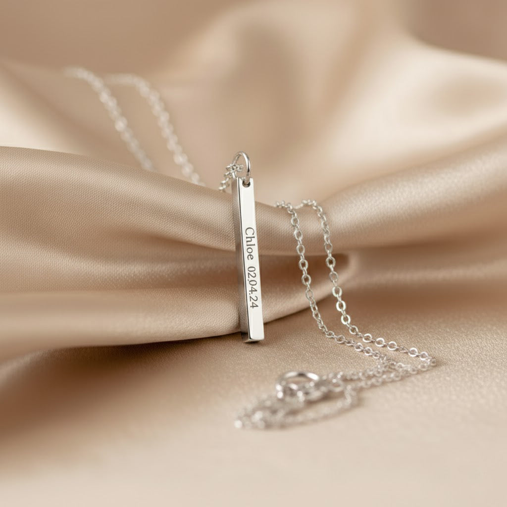 A minimalist sterling silver bar pendant etched with exact latitude longitude necklace details, styled on a soft backdrop with prism light. This slim GPS coordinates necklace turns a special place—first date, proposal spot, new home—into elegant location jewelry. Deep laser text runs along one face of the bar for a modern engraved coordinate bar look; perfect as a travel keepsake gift or anniversary memento with custom map coordinates and adjustable chain length.