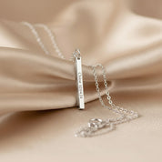 A minimalist sterling silver bar pendant etched with exact latitude longitude necklace details, styled on a soft backdrop with prism light. This slim GPS coordinates necklace turns a special place—first date, proposal spot, new home—into elegant location jewelry. Deep laser text runs along one face of the bar for a modern engraved coordinate bar look; perfect as a travel keepsake gift or anniversary memento with custom map coordinates and adjustable chain length.