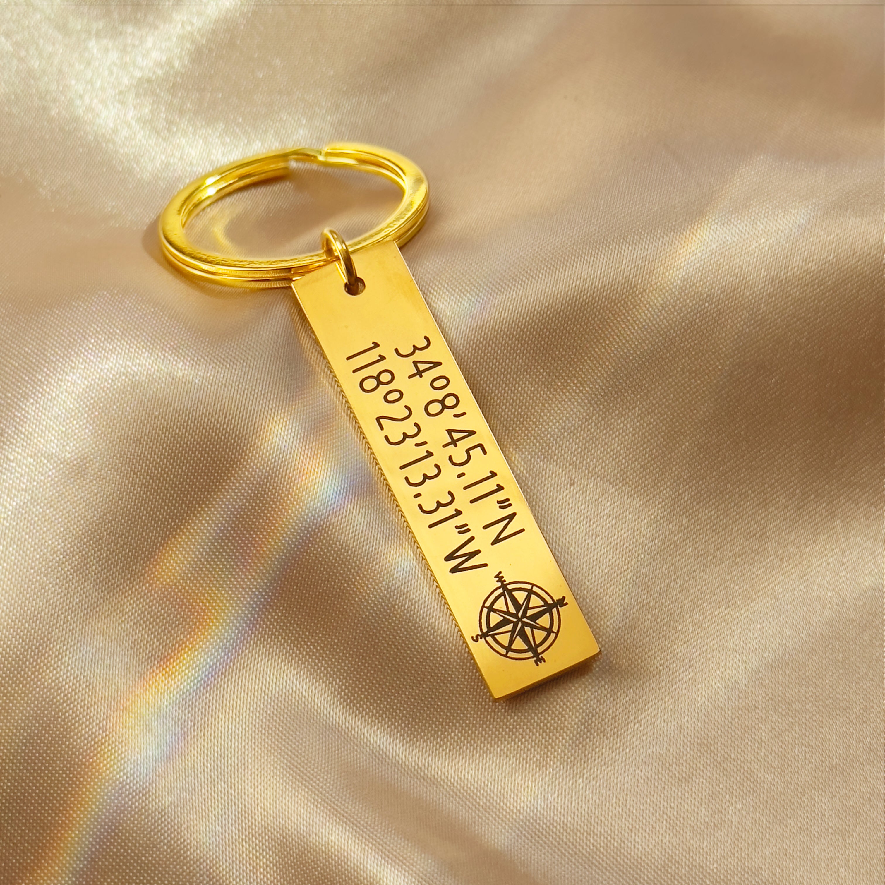 A trio of engraved GPS coordinates bar keychains in silver, gold and black stainless steel displayed on satin, personalized with names, dates and location coordinates; modern rectangular custom bar design with split ring; personalized keychain, engraved keychain, custom key chains, stainless steel keychain, couples keychain; ideal anniversary or wedding gift for him, groomsmen gift keychain; gift-ready packaging included.