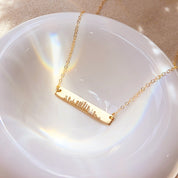 Custom gold skyline bar necklace on iridescent dish, engraved city silhouette pendant, personalized travel jewelry gift for women.