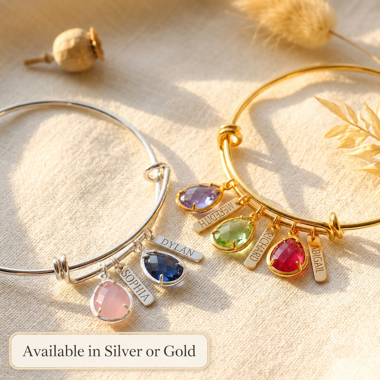 Personalized birthstone bangles hanging in soft natural light, showing colorful gemstone and engraved name charm options in silver or gold