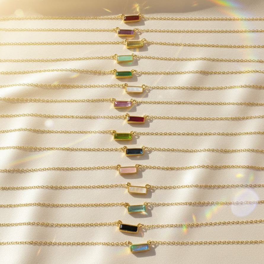 Assorted Tiny Adira birthstone bar necklaces arranged together to display all twelve gemstone options, including amethyst, garnet, aquamarine, citrine, sapphire, peridot, and more. Features gold vermeil chains and petite bar connectors. Personalized minimalist necklace with optional engraving, perfect for birthdays, bridesmaids, anniversary gifts, and custom jewelry lovers.