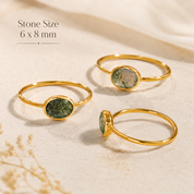 Three gold rings with oval green stone inlays are arranged on a light beige textured surface. Text in the upper left reads 'Stone Size 6 x 8 mm'.