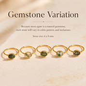 Five gold rings with oval moss agate stones are lined up on a light beige textured surface. Text above reads 'Gemstone Variation' with a note explaining that each stone will vary in color, pattern, and inclusions, and that the stone size is 6 x 8 mm.