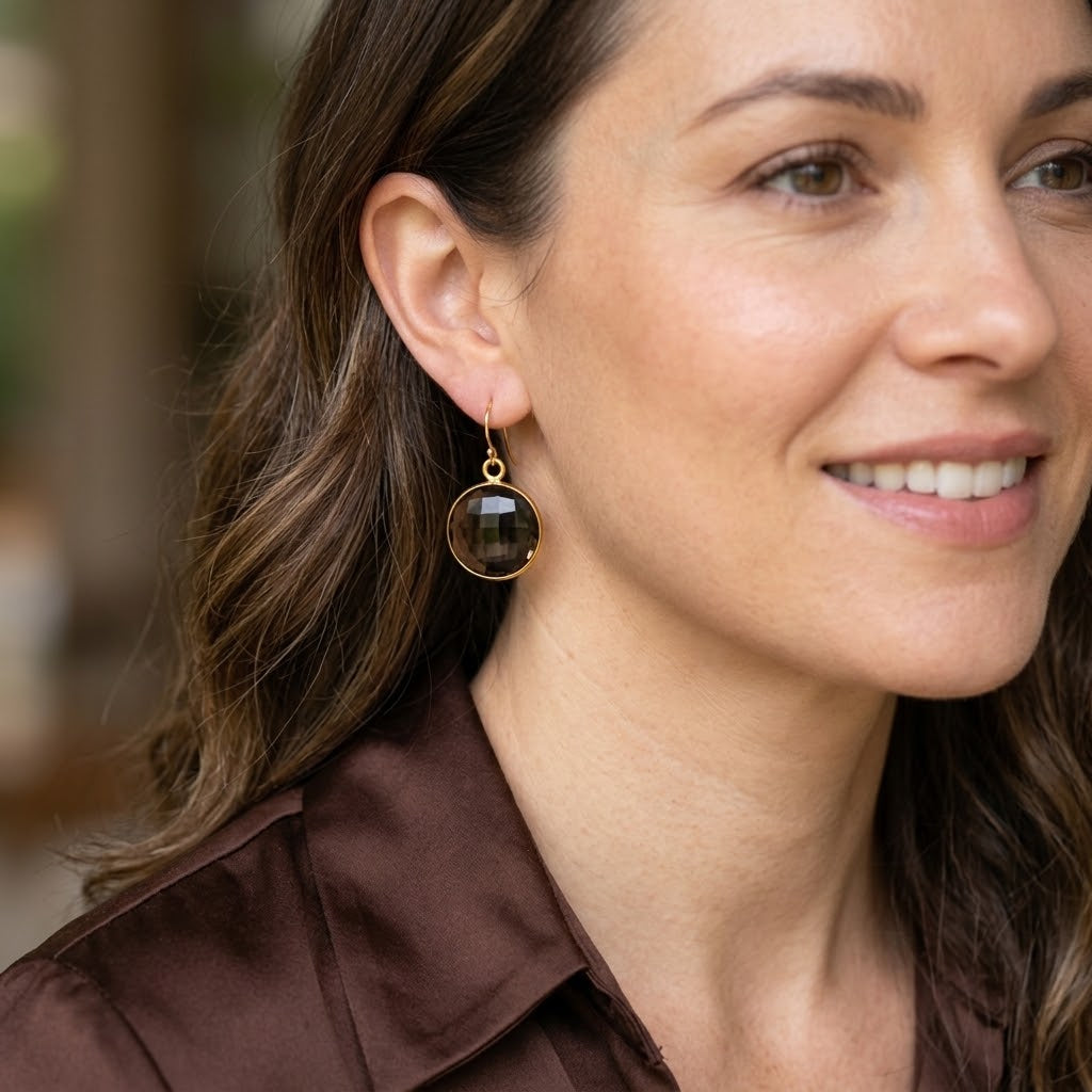 Woman wearing large round Smoky Quartz drop earrings in gold with warm brown faceted gemstones.

