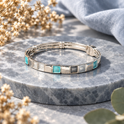 Silver Mosaic Squares bangle bracelet with teal and gray accents displayed on gray stone

