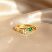 pair of dainty stackable birthstone rings with slim gold bands resting on softly draped champagne satin, one bezel set with a pale icy aqua stone and the other with a rich emerald green gemstone, showcasing the minimalist design of these thin aqua chalcedony and green birthstone rings, perfect for creating a personalized march birthday stack or meaningful mom ring set, handmade in sterling silver or gold vermeil for everyday wear or gifting