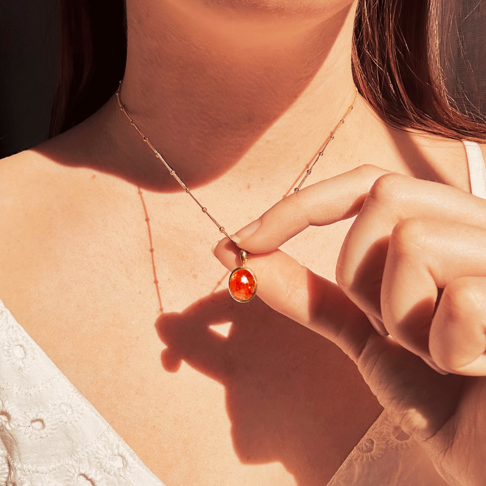 Model wearing a white lace blouse holds Dainty Large Oval Sunstone Bezel Set Pendant on a gold filled satellite chain. Sunstone Jewelry Necklace, Natural Orange Sunstone, Celestial Sun Jewelry, Summer Birthday