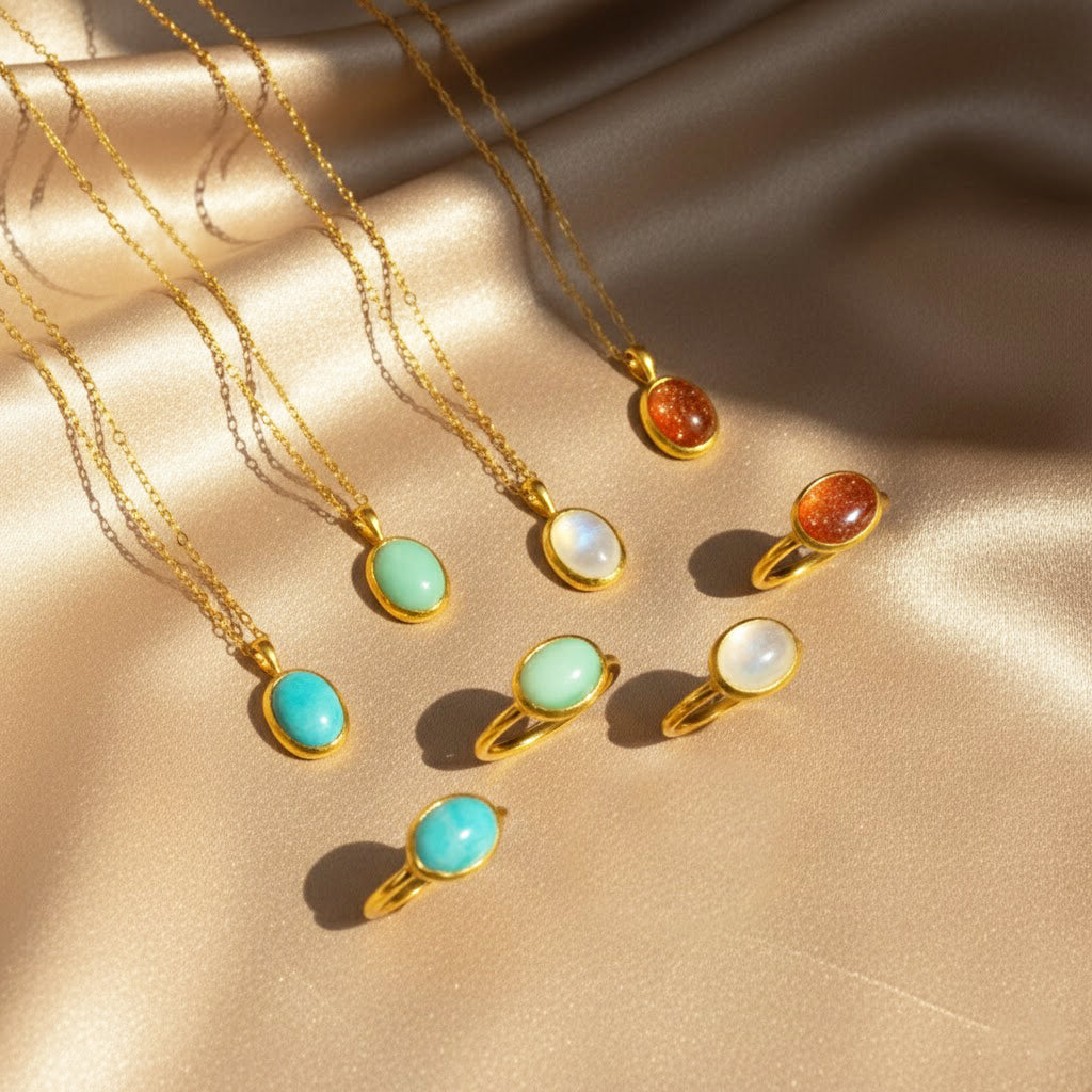 Elegant collection of matching oval gemstone necklaces and rings displayed on shimmering champagne satin, featuring bezel-set stones in moonstone, turquoise, green chalcedony and goldstone with rich gold settings. Coordinated gemstone jewelry set ideal for gifting or mix-and-match styling, perfect for birthdays, anniversaries, Mother’s Day or Christmas, offering minimalist everyday wear pieces for her, mom, sister or best friend.
