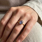 Close-up of natural Tanzanite oval cabochon ring worn on the hand with a delicate gold band.
