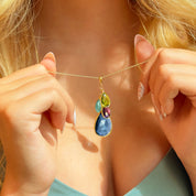 Custom birthstone mom necklace shown on model, with a large navy teardrop gemstone framed in gold and topped by three petite bezel-set birthstones (peridot green, aquamarine blue, amethyst purple) on a delicate gold chain. Personalized family birthstone pendant for mothers—add kids’ stones and initials; available in gold filled or sterling silver. A meaningful Mother’s Day, Christmas, birthday, or push present keepsake, dainty everyday mom jewelry, handcrafted and gift-ready.